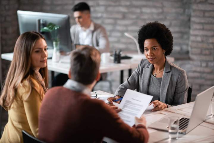 african american financial advisor going through paperwork with her clients while having meeting office